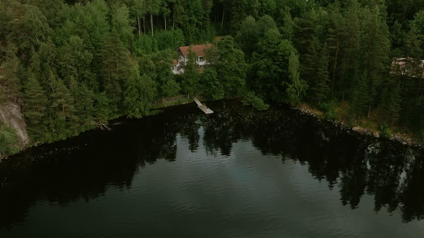 Aerial view of a house by a lake with a wooden dock surrounded by dense forest in Hameenlinna, Kanta-Hame, Finland.