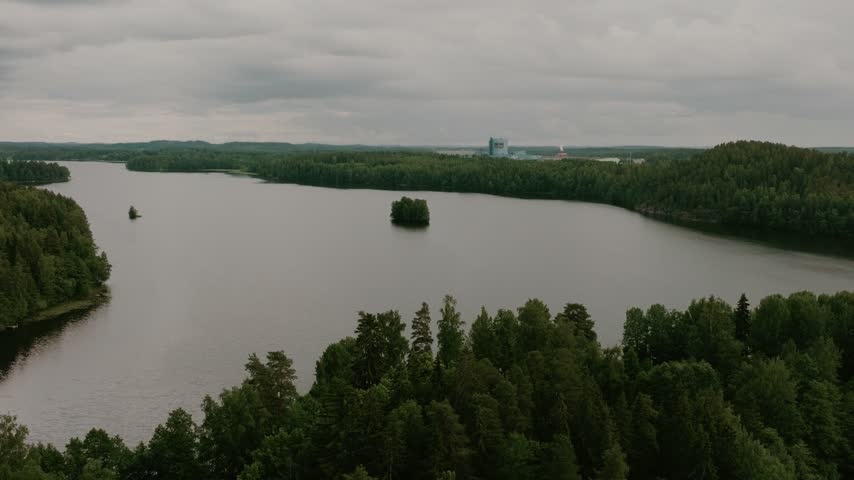 Aerial view of a serene lake surrounded by dense pine forests under a cloudy sky in Hameenlinna, Kanta-Hame, Finland.