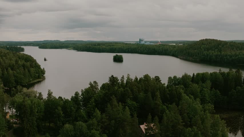 Aerial view of a serene lake surrounded by dense pine forests and a small island under a cloudy sky in Hameenlinna, Kanta-Hame, Finland.