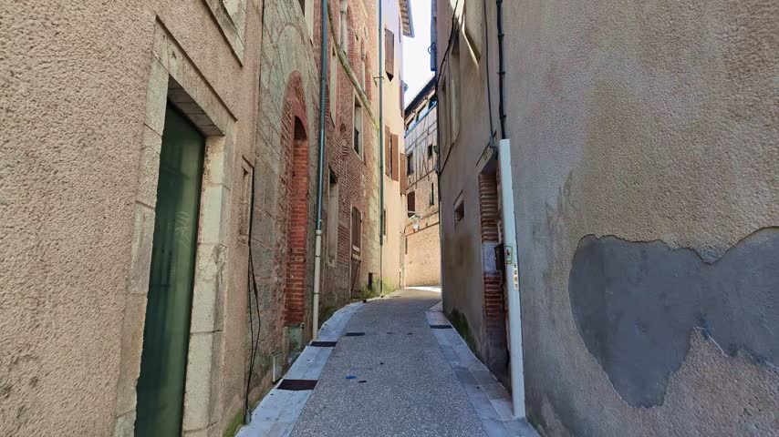 Walking shot through narrow historic streets of Cahors old town in bright sun.