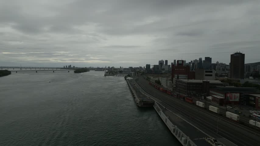 Montreal port and downtown skyline near Jacques Cartier bridge, St. Lawrence river, rail yard and shipping containers under grey clouds, Quebec, Canada.