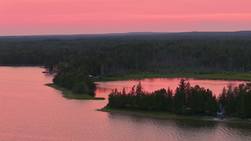 Aerial panorama of wooded shoreline points and sheltered water beneath a vivid pink sunset sky near Hessel Michigan