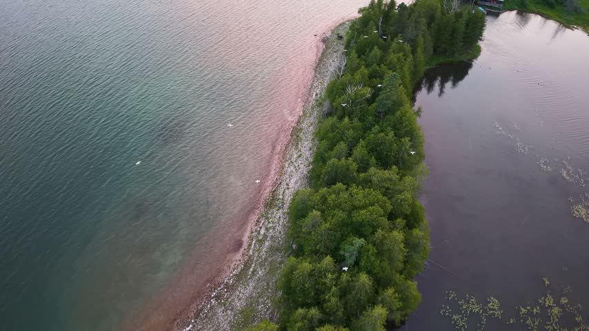 Aerial view along a narrow wooded shoreline with a rocky beach separating open water from a sheltered inlet near Hessel Michigan