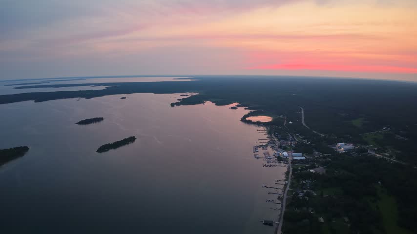 Aerial view of wooded islands and the Hessel shoreline beside calm water reflecting a colorful orange sunset in Michigan