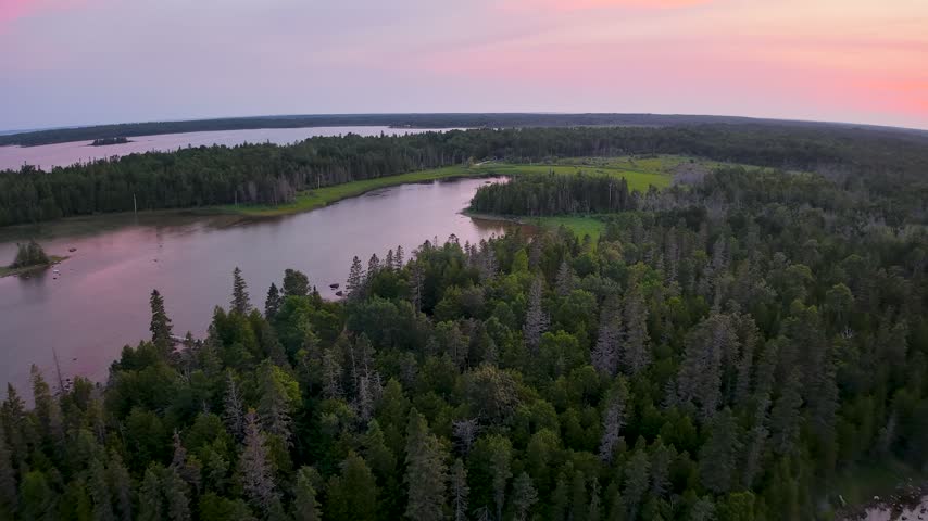 Aerial panorama of a calm inlet bordered by forest and wetlands beneath a pink sunset sky near Hessel in the Upper Peninsula of Michigan