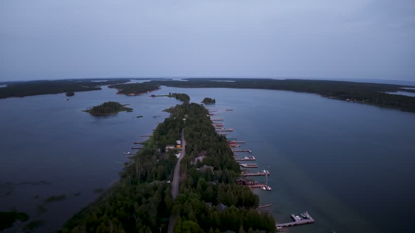 Drone view of a road running through a wooded island lined with waterfront homes and docks near Hessel Michigan