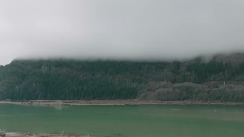Footage of fog covered mountains and evergreen forest above calm green water at The Spit in Squamish British Columbia Canada