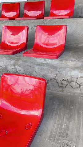 Eager anticipation before the game as rows of empty glossy red plastic seats line the concrete bleachers of a stadium