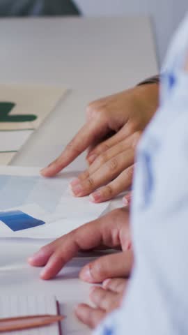 Vertical video: Bringing green pencil, designer pointing to blue swatches in office. Collaboration, palette, notepad, scissors, watch, glass, vertical video
