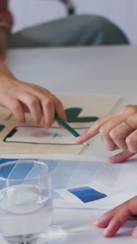 Vertical video: Hands pointing at mockup chips at table, selecting color with green pencil pink top. Collaboration, design, swatches, palette, layout, duo, vertical video