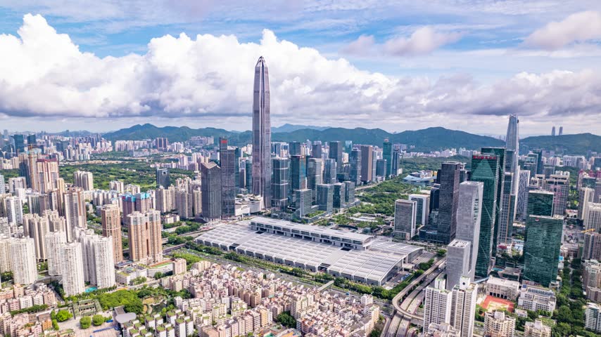 Aerial view of exhibition halls amid a dense business skyline in Shenzhen, Guangdong, China. The scene features Shenzhen Convention and Exhibition Center. Time-lapse footage. Relevant to venue architecture and urban development.
