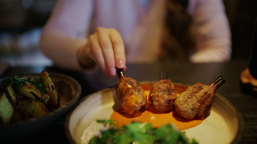Young woman enjoying gourmet lamb skewers with red pepper dip and herb salad at a stylish fine dining establishment.