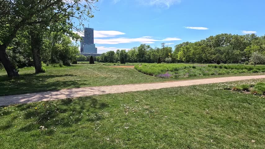 Vibrant green lawns and manicured paths stretch across Donau Park with tall modern buildings rising in the clear blue sky behind and lush trees framing the scene.
