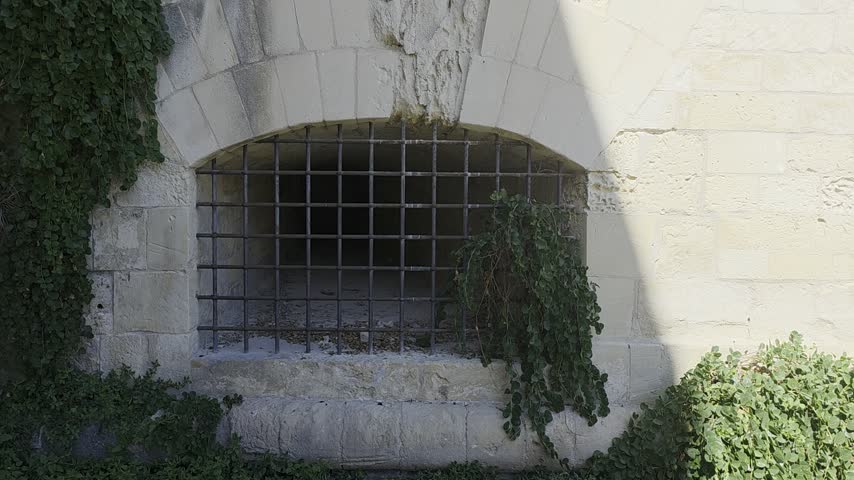 Camera moving through a metal grid window into an ancient stone tunnel inside a medieval fortress, close up.