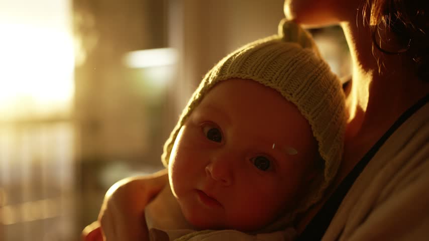Close up of a happy infant in a warm knitted hat, cradled in its mother