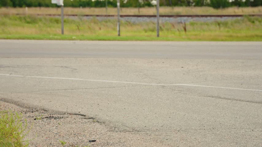 Panning up shot of a green and white provincial highway sign outside Watrous, Saskatchewan, showing directions to Moose Jaw and Prince Albert as a car passes in the foreground