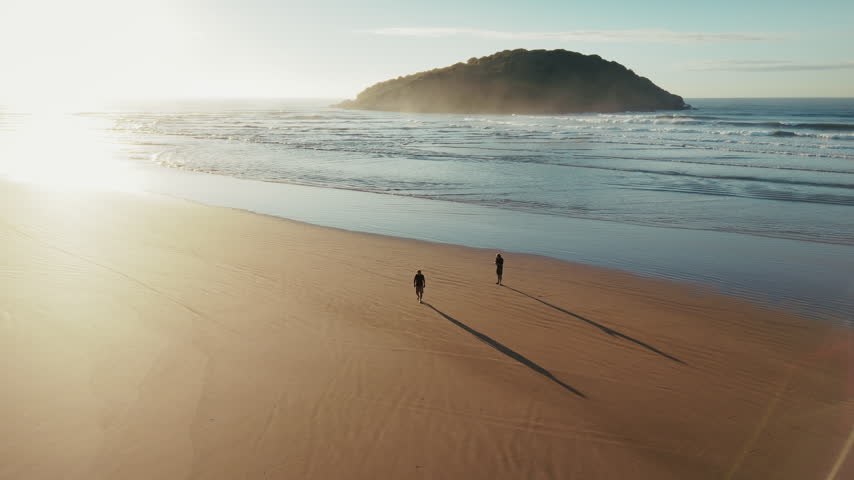 Two persons walk on the wide sandy beach with island on the horizon.