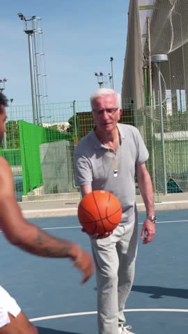 Experienced referee throwing the ball up for a tip off between two opposing players, starting a competitive basketball game on a sunny day