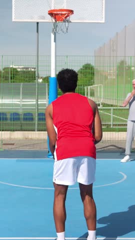 Slow motion view of a young basketball player scoring during an outdoor game with friends. The group of men enjoys playing on a sunny day