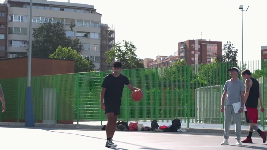 Group of young men playing basketball on a sunny day. Player dribbling, shooting, and scoring while a defender tries to block him