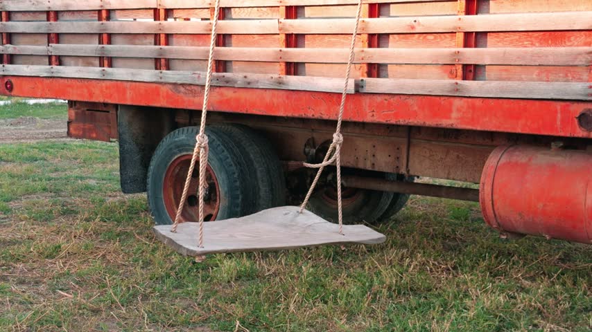 A wooden rope swing sways slowly beside the rear wheel of a parked truck.