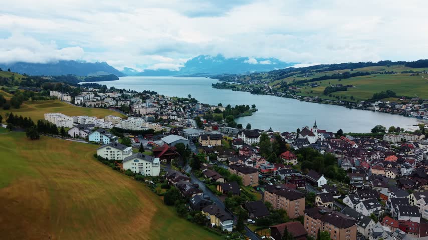 Drone climbs above fields beside Kussnacht, widening the view over Lake Lucerne.