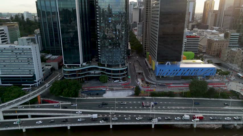 Camera tilts up from traffic along the Brisbane River to the top of The One skyscraper at Brisbane Quarter during sunrise in Queensland, Australia.