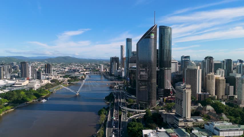 Aerial trucking shot of the Brisbane CBD skyline, 1 William Street tower, and the Brisbane River under a clear morning sky in Queensland, Australia.