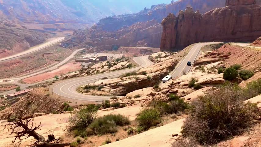 RV travels a winding scenic road through the dramatic red rock canyons of Arches National Park in Utah, showcasing desert scenery and American road trip travel.