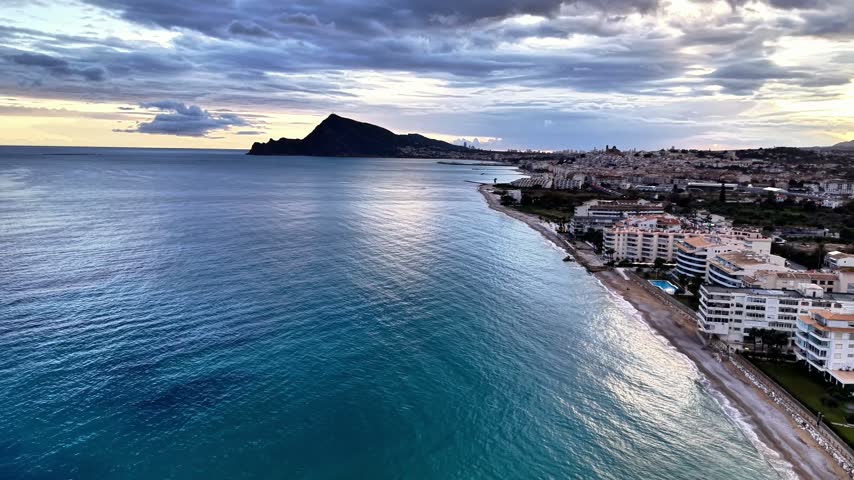 Morning Shoreline With Shimmering Reflections, Aqua Sea, Quiet Promenade, Resort Rooftops And Soft Sunrise