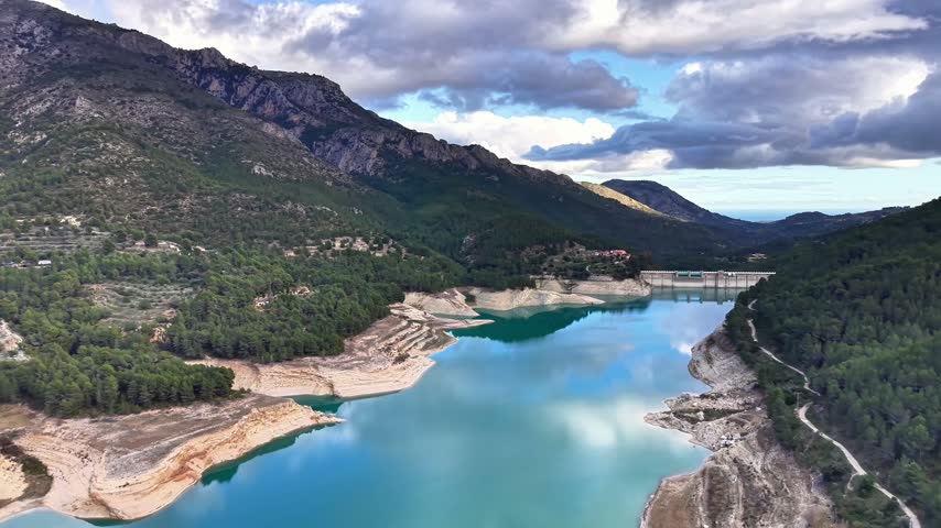 Panoramic Reservoir With Dramatic Sky And Mirrorlike Reflections Across Turquoise Water, Surrounded By Rugged