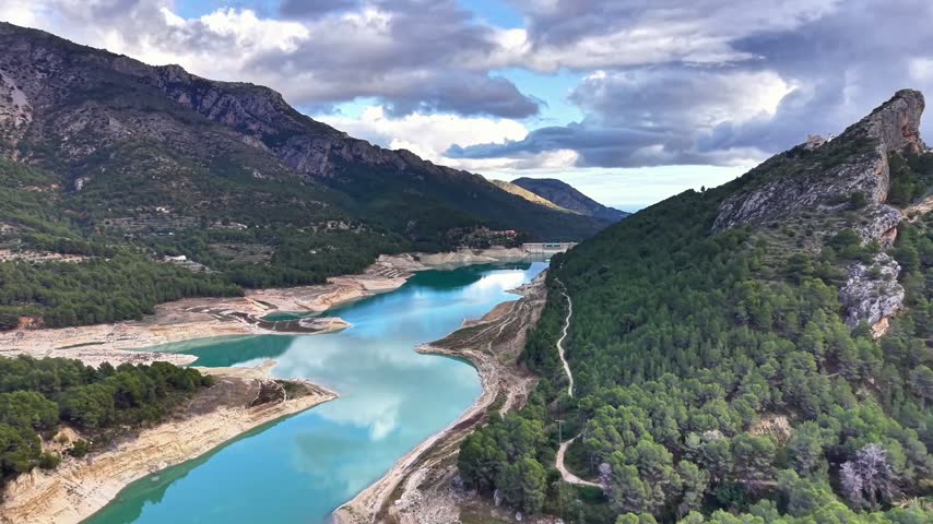 Aerial River Corridor Winding Through Steep Banks And Dense Pine Forest With Turquoise Water And Reflective