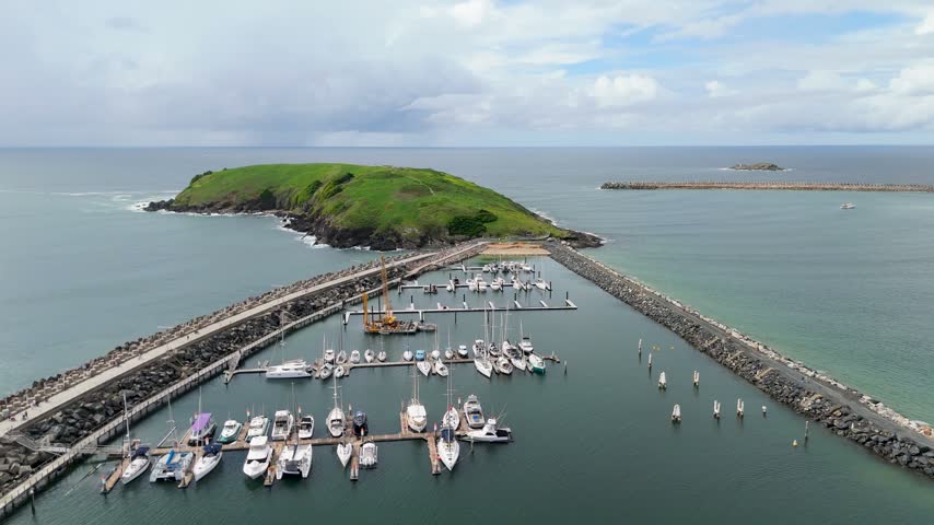 Aerial push in shot over boats docked at Coffs Harbour Marina toward scenic Muttonbird Island and the Pacific Ocean in New South Wales, Australia.