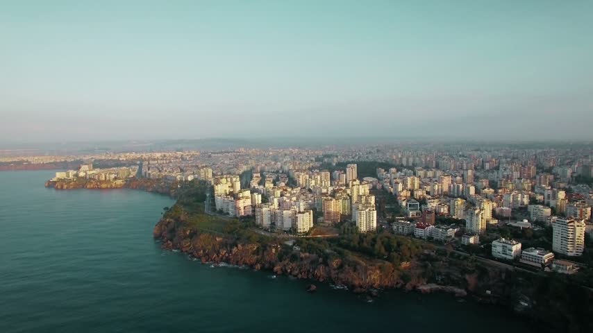 Antalya Turkey ocean and buildings showcases the stunning Mediterranean coastline of Antalya, featuring crystal-clear blue waters, modern buildings, coastal resorts, and scenic urban architecture. This beautiful aerial and landscape footage captures the unique combination of turquoise sea, waterfront properties, residential neighborhoods, and the vibrant atmosphere of one of Türkiye’s most popular seaside destinations. Located along the Turkish Riviera, Antalya is renowned for its beaches, tourism industry, picturesque coastline, and breathtaking views of the Mediterranean Sea. The footage highlights the relationship between the natural coastal environment and the city’s expanding urban landscape, making it ideal for travel documentaries, tourism promotions, hotel advertisements, real estate presentations, and commercial video productions. The contrast between blue ocean waters and city buildings creates an appealing visual for projects focused on summer holidays, luxury resorts, coastal living, architecture, and international travel. Suitable for travel guides, social media videos, promotional campaigns, and educational content, these visuals capture the beauty and charm of Antalya’s Mediterranean setting while showcasing its distinctive waterfront scenery and modern city environment.