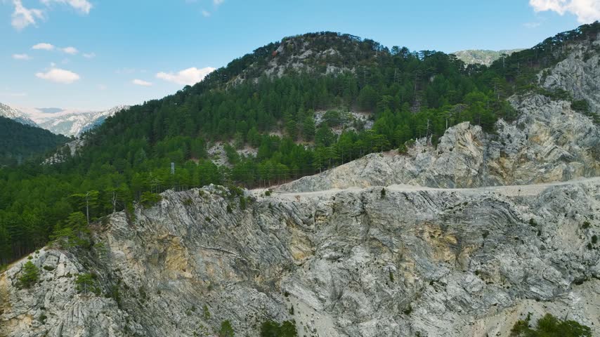 Video showing a winding road carved into rocky mountain hills with green trees on top under a — Taurus Mountains, Antalya, Turkey
