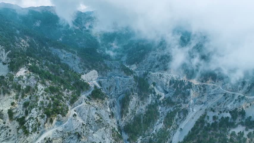 Aerial footage of a rocky mountain area partially covered with fog, featuring a curving road — Taurus Mountains, Antalya, Turkey