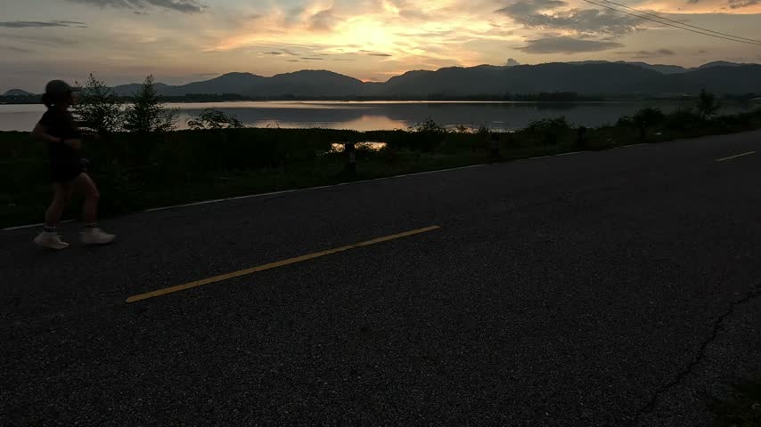 Silhouettes of people exercising on a public dam crest; a runner exercising on the paved road atop the dam.