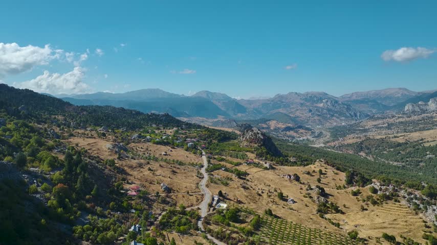 Aerial view of a mountainous landscape featuring a winding road, scattered houses, trees, and — Taurus Mountains, Antalya, Turkey