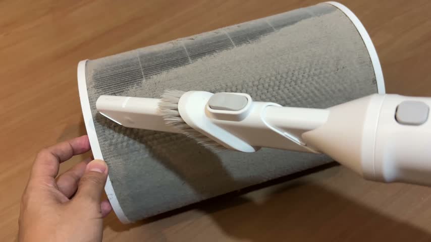 Cleaning thick dust and lint from a dirty cylindrical air purifier filter with a vacuum cleaner brush attachment