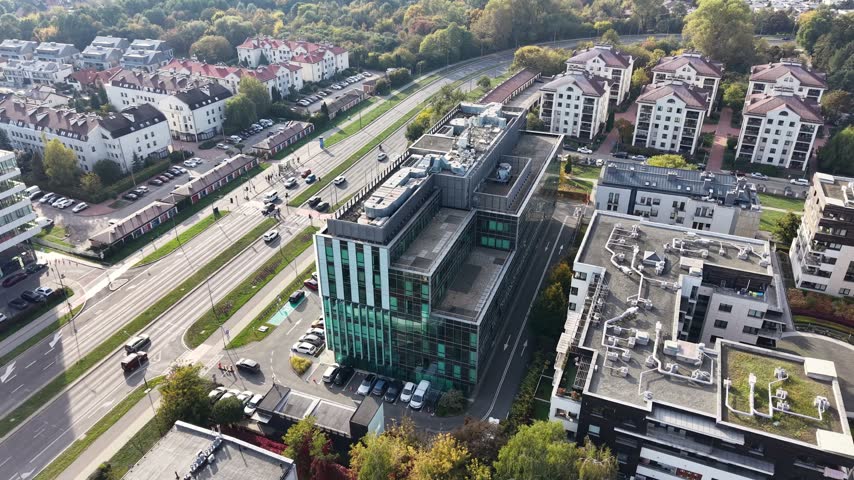 Aerial view of modern office buildings and traffic along a busy city street with tram tracks, rooftop equipment, parked cars, and surrounding urban neighborhoods