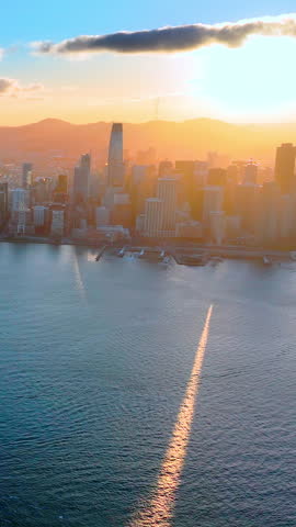 San Francisco sunset cityscape and golden bay reflection, California. Urban skyline silhouetted against glowing sunset sky with sparkling water trail. Vertical video.