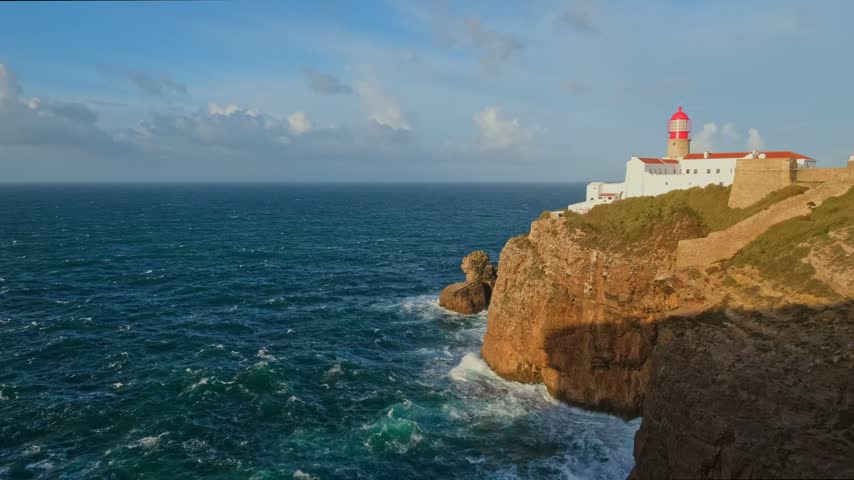 View of the Lighthouse of Cabo de Sao Vicente in Sagres, Algarve, Portugal, at sunrise with Atlantic ocean, cliffs, and from camera morning sea