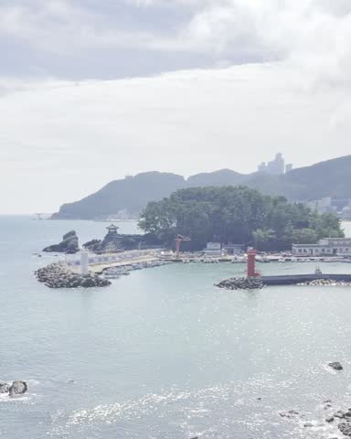 Scenic view of a coastal harbor with lighthouses, calm blue water, rocky shoreline and green mountains in the background.