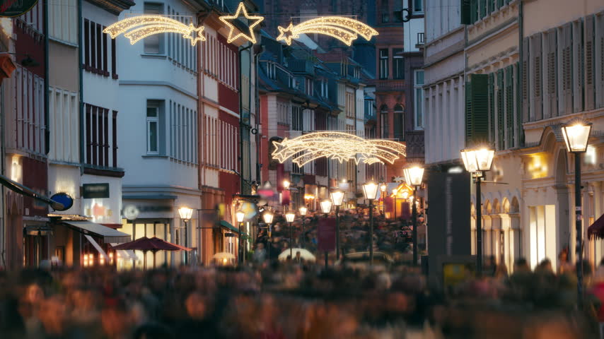 Loads of people with motion blur rushing and shopping on the historic German city of Heidelberg at Christmas. With holiday decoration shining lamp posts.