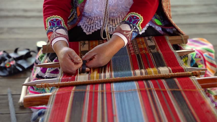 Slow-motion close-up of Andean hands weaving while wearing colorful traditional Peruvian clothing