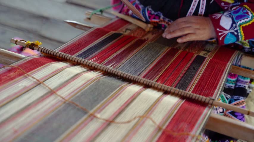 Slow-motion close-up of Andean hands weaving while wearing colorful traditional Peruvian clothing