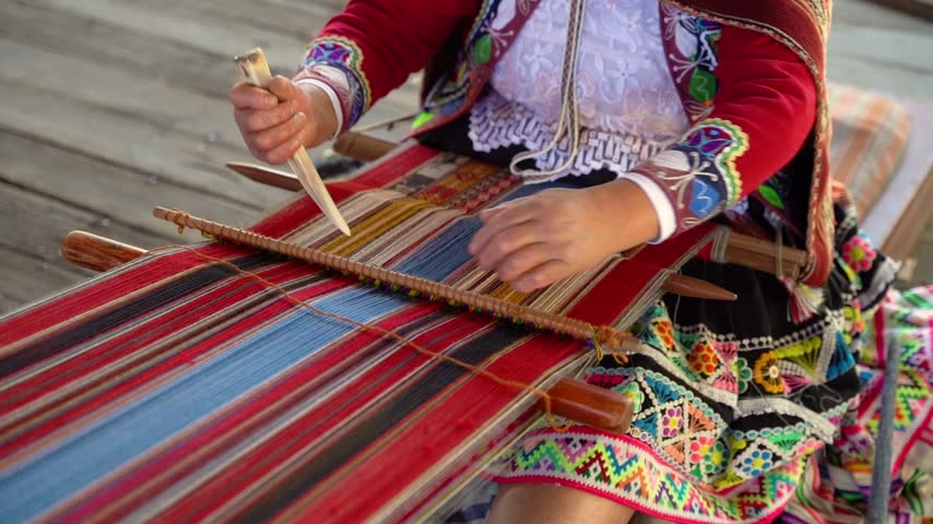Slow-motion close-up of Andean hands weaving while wearing colorful traditional Peruvian clothing