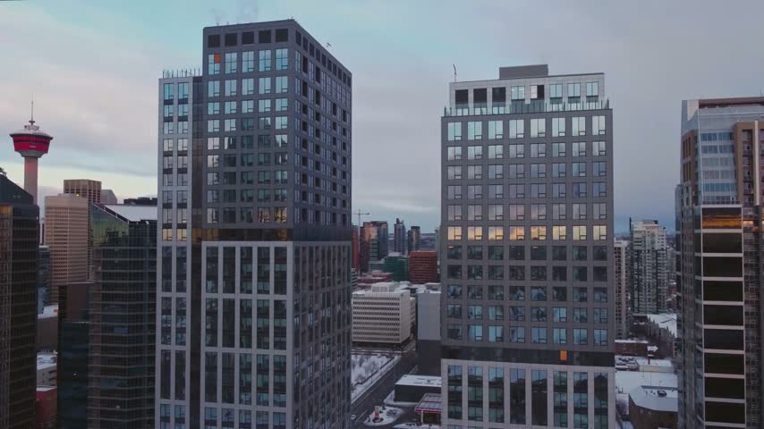 Wide high-angle panoramic aerial perspective overlooking the high-density corporate office towers and residential buildings of the central business district in Calgary, Alberta, Canada, showcasing the iconic Calgary Tower under a soft sunset gradient twilight sky with snow-dusted grounds.