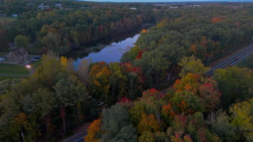 Aerial view of Stanley Quarter Park in New Britain, Connecticut, USA, showcasing a winding road, tranquil lake, and vibrant autumn foliage. 4K footage.