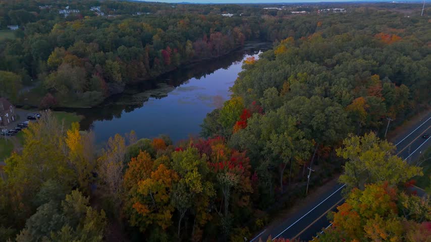 Aerial view of Stanley Quarter Park in New Britain, Connecticut, USA, featuring a calm lake reflecting the sunset sky amid colorful autumn foliage. 4K.